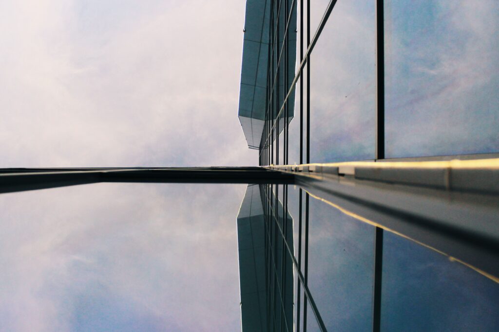 Low angle view of a modern glass building reflecting the sky, showcasing contemporary architectural design in an urban setting.